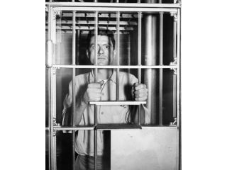 Portrait of a mid adult man standing behind prison bars Poster Print (18 x 24)