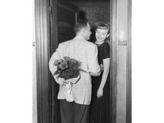 Rear view of mid adult man standing with mid adult woman at doorway, hiding bouquet of flowers behind back Poster Print